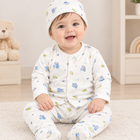 A smiling baby sitting on a white carpet wearing a matching footed sleeper outfit and bonnet with a blue and green cartoon animal print on a white background.